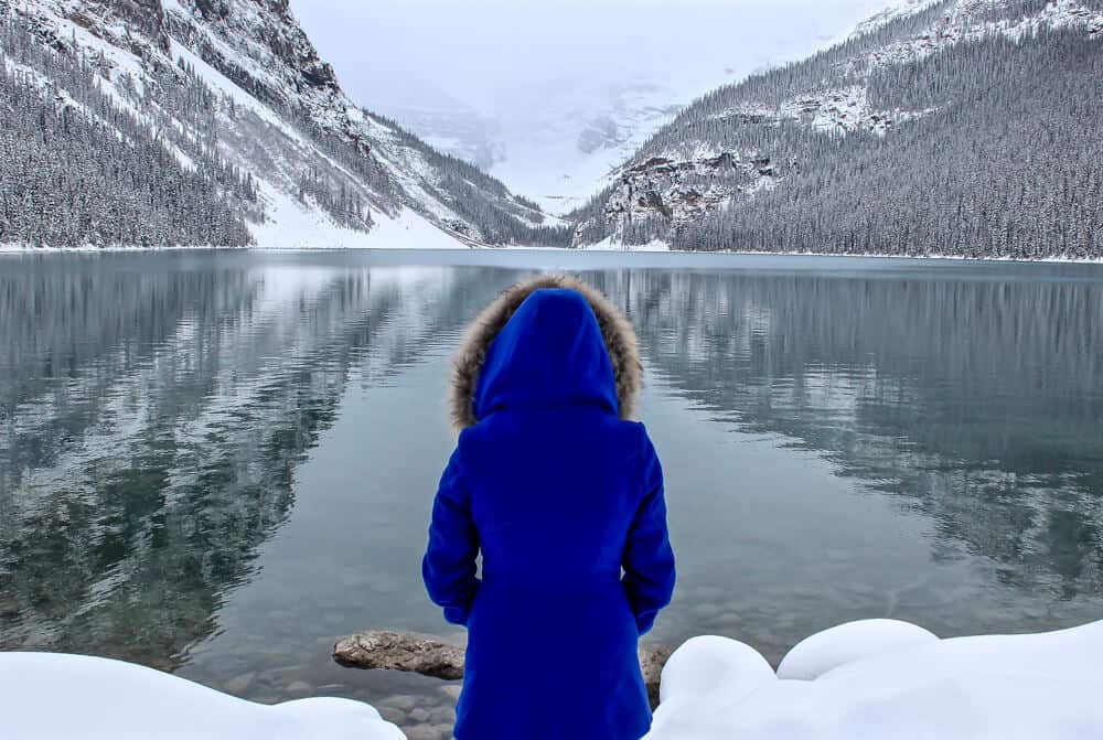 lora wearing a bright blue winter jacket standing in front of lake louise. the mountains in the background are covered in snow.