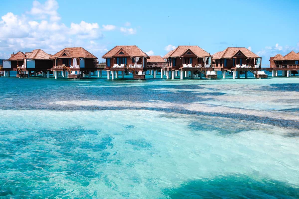 five brown overwater bungalows lined up over turquoise water  in jamaica
