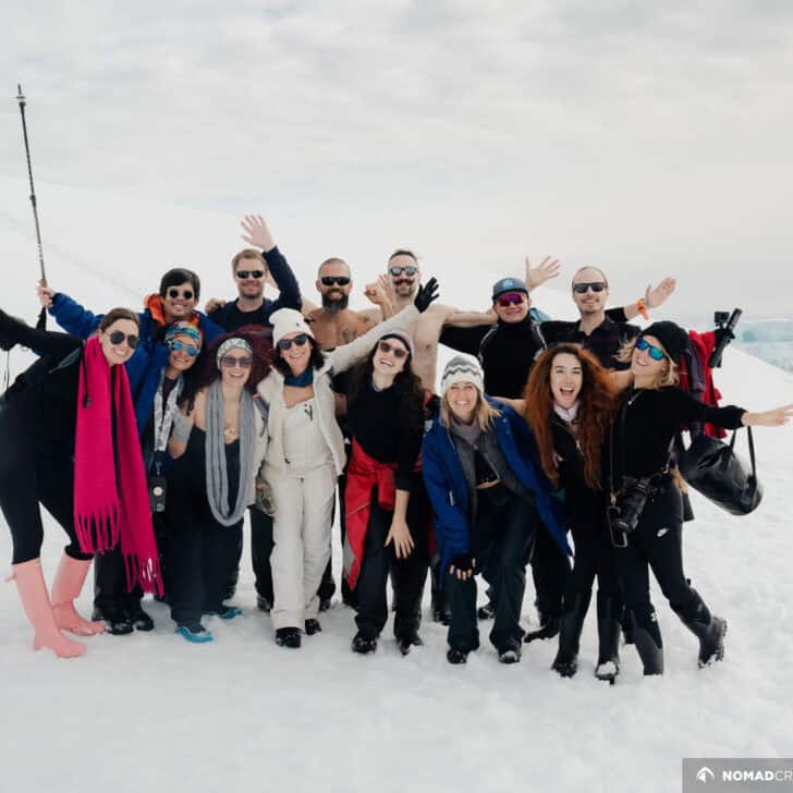A group of joyful people in varied attire posing together on a snowy landscape with icebergs in the background.