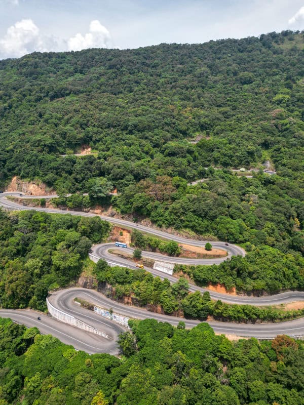 Aerial view of a winding, mountainous road surrounded by dense greenery and forested hills.