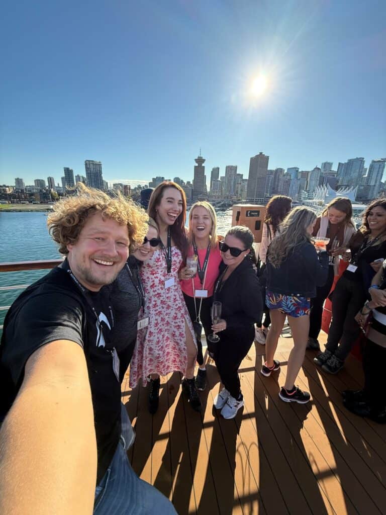 A group of people on the boat deck savor a sunny day, city skyline stretching behind them. As they hold drinks and beam at the camera, it's evident their nomad cruise review would be nothing short of glowing.