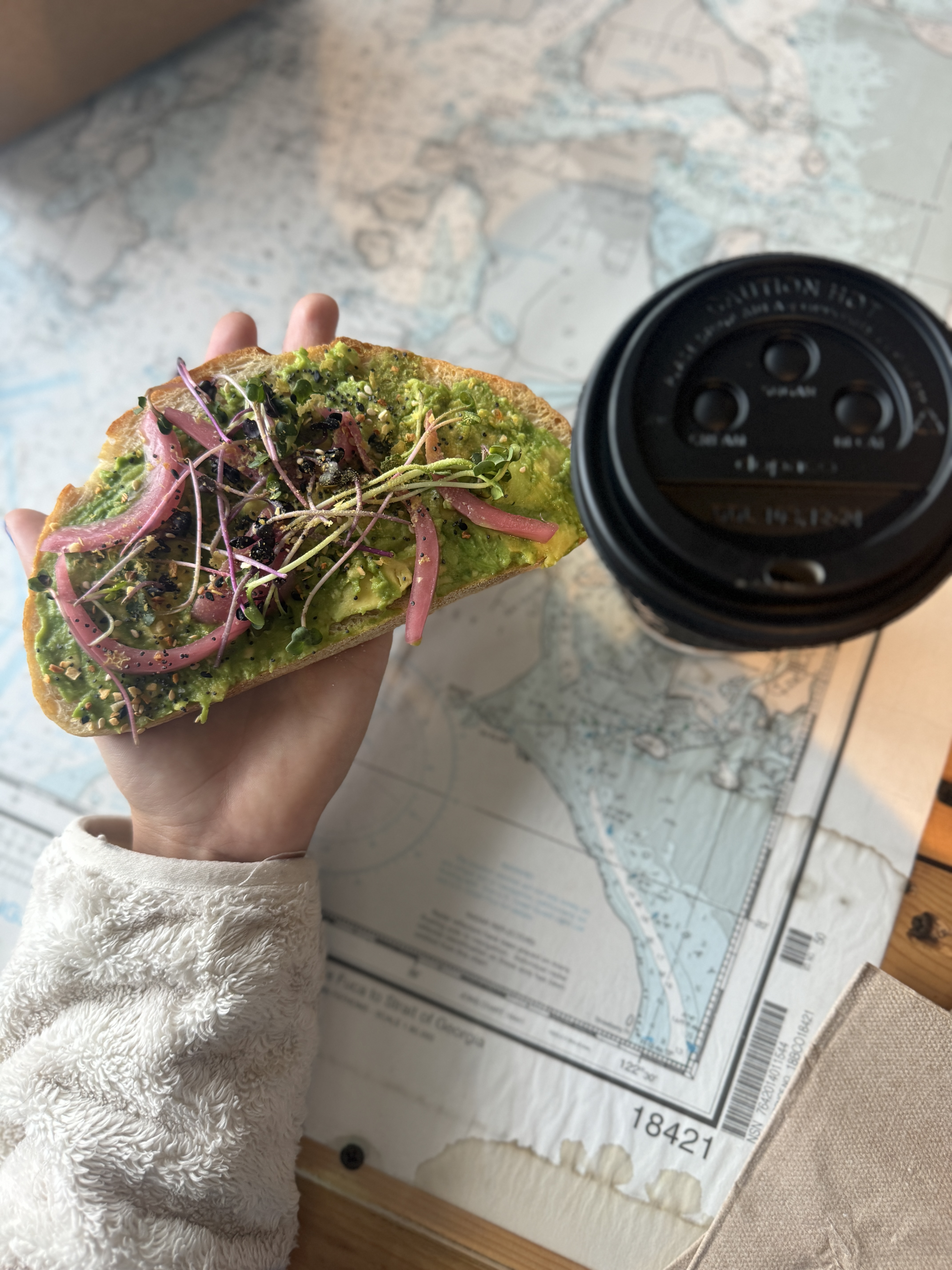 hand holding avocado roast next to a coffee over a map