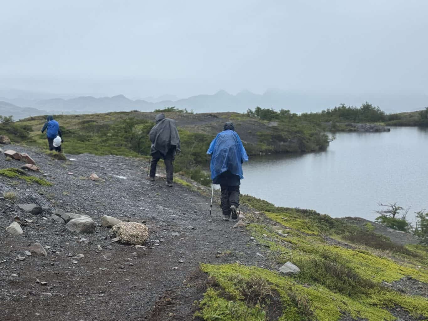 hikers wearing rain gear walking across a rocky path in torres del paine w trek