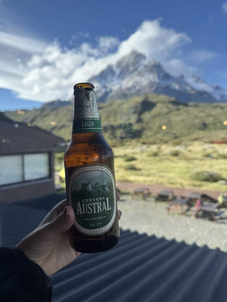 a person holding a chilean beer in front of a mountain peak with clouds above it