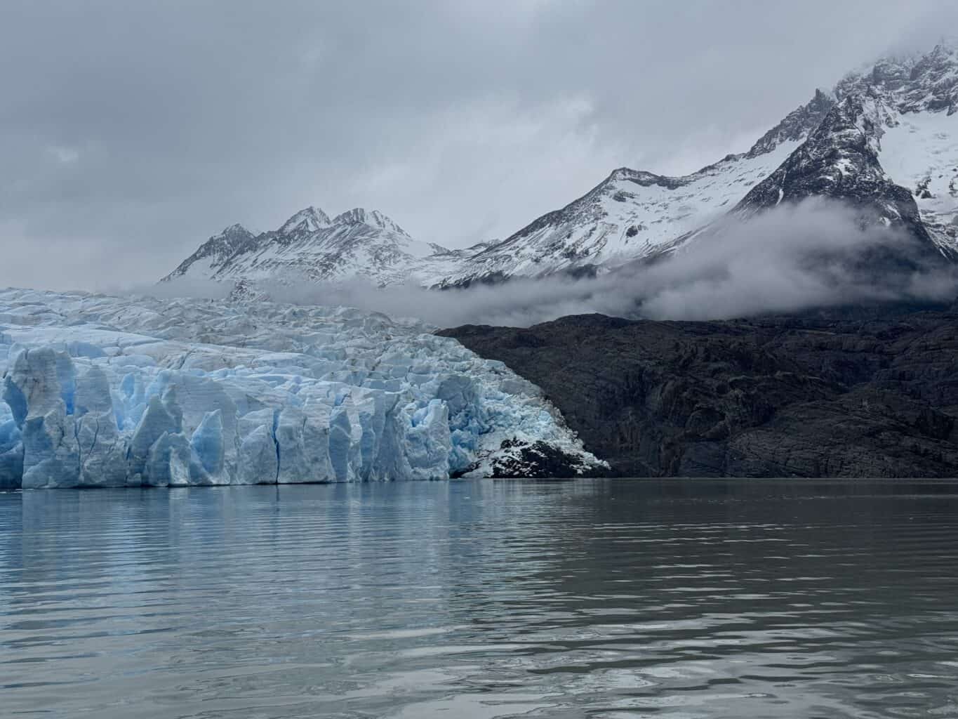 a blue glacier with a moody mountain behind it and a grey sky in patagonia