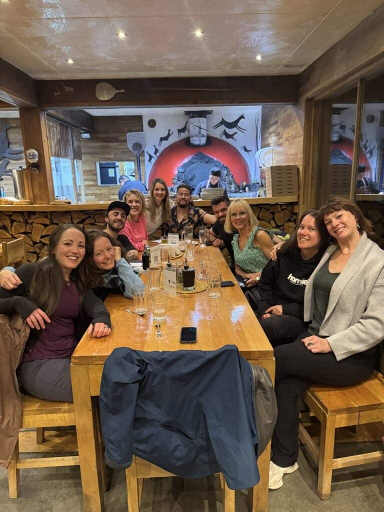 A group of people smiling and sitting around a table with drinks in a wood-paneled restaurant.