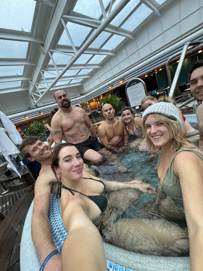 A group of people relaxing in a hot tub under a glass ceiling, with some smiling at the camera.