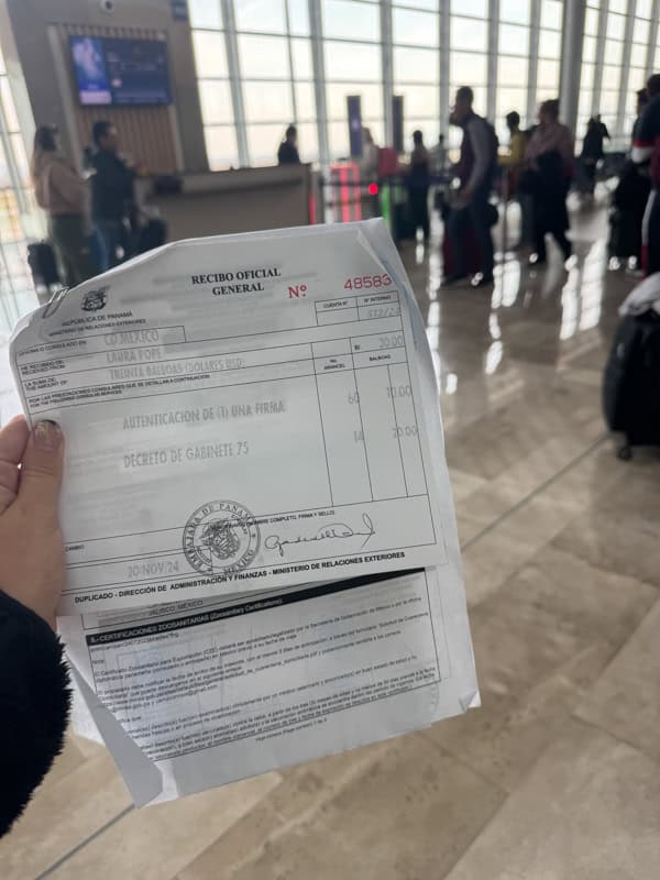 A person holds an official document in an airport, with travelers and luggage visible in the background.